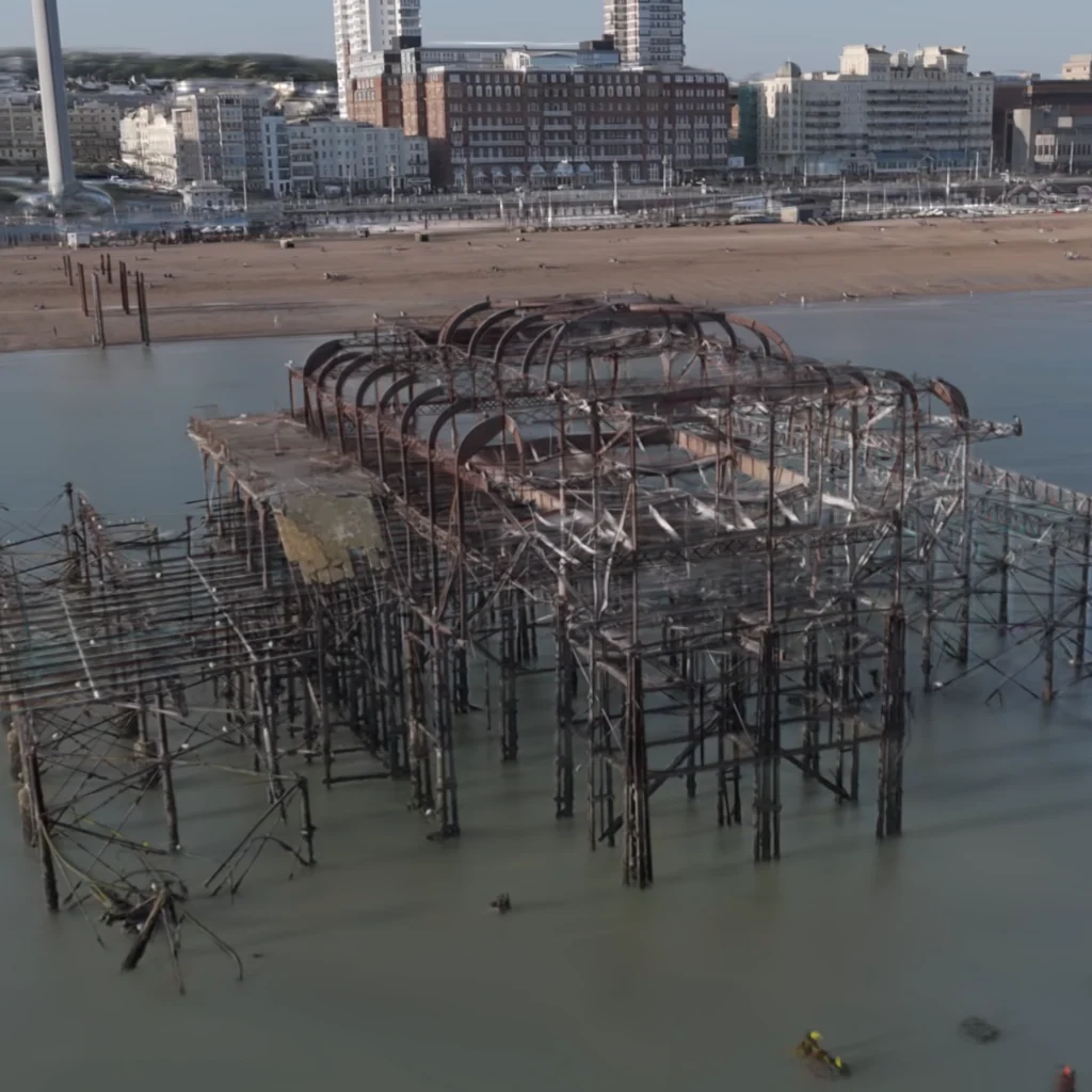 Aerial reconstruction of Brighton West Pier's exposed framework, with the beach and seafront behind it.