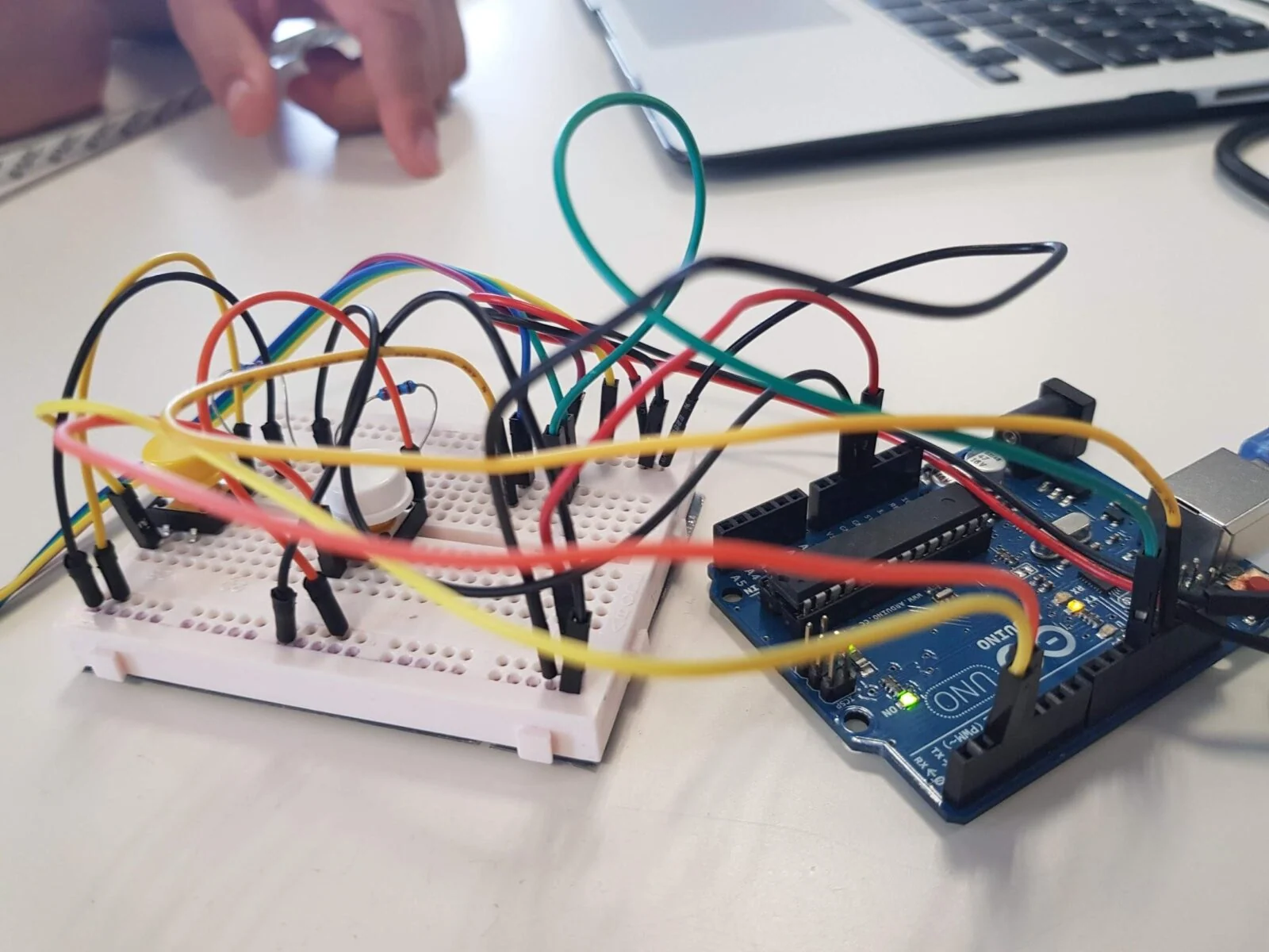Arduino board connected to a breadboard with multicoloured jumper wires beside a laptop.