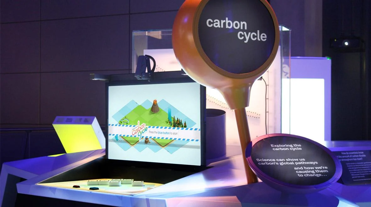 Carbon Cycle museum exhibit with a screen, tabletop controls and a round orange sign.