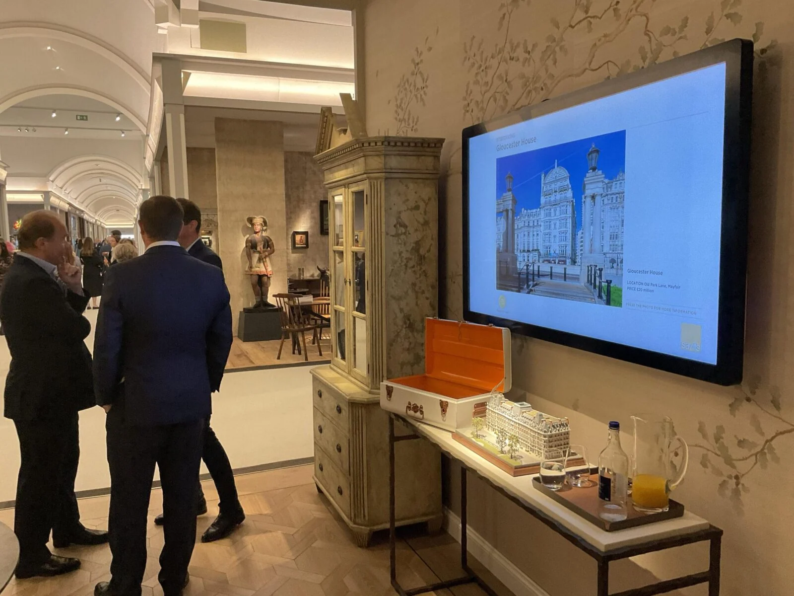 Visitors beside an architectural display screen and scale models at Masterpiece fair.