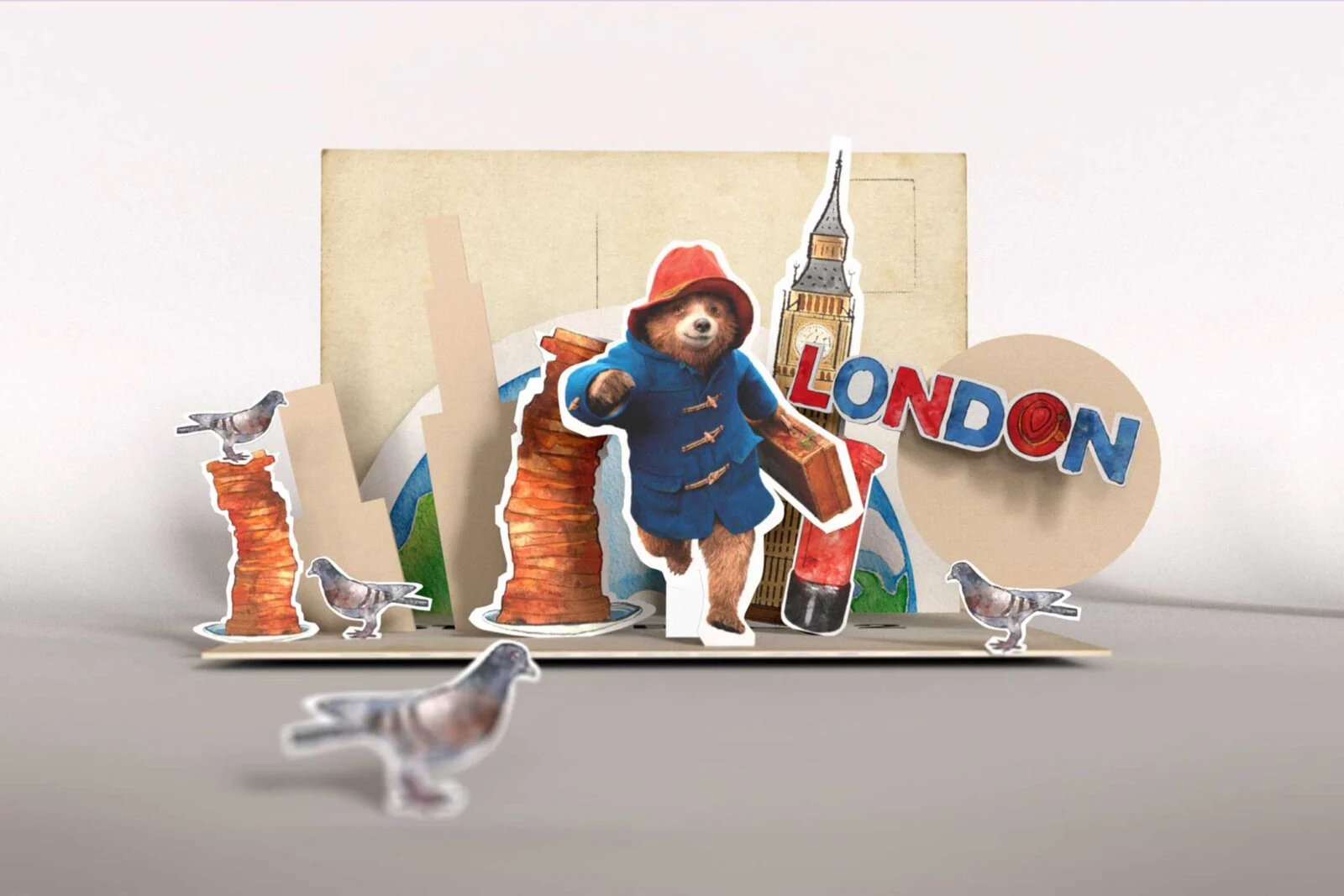 Paddington carrying a suitcase in a pop-up London scene with pigeons and Big Ben.