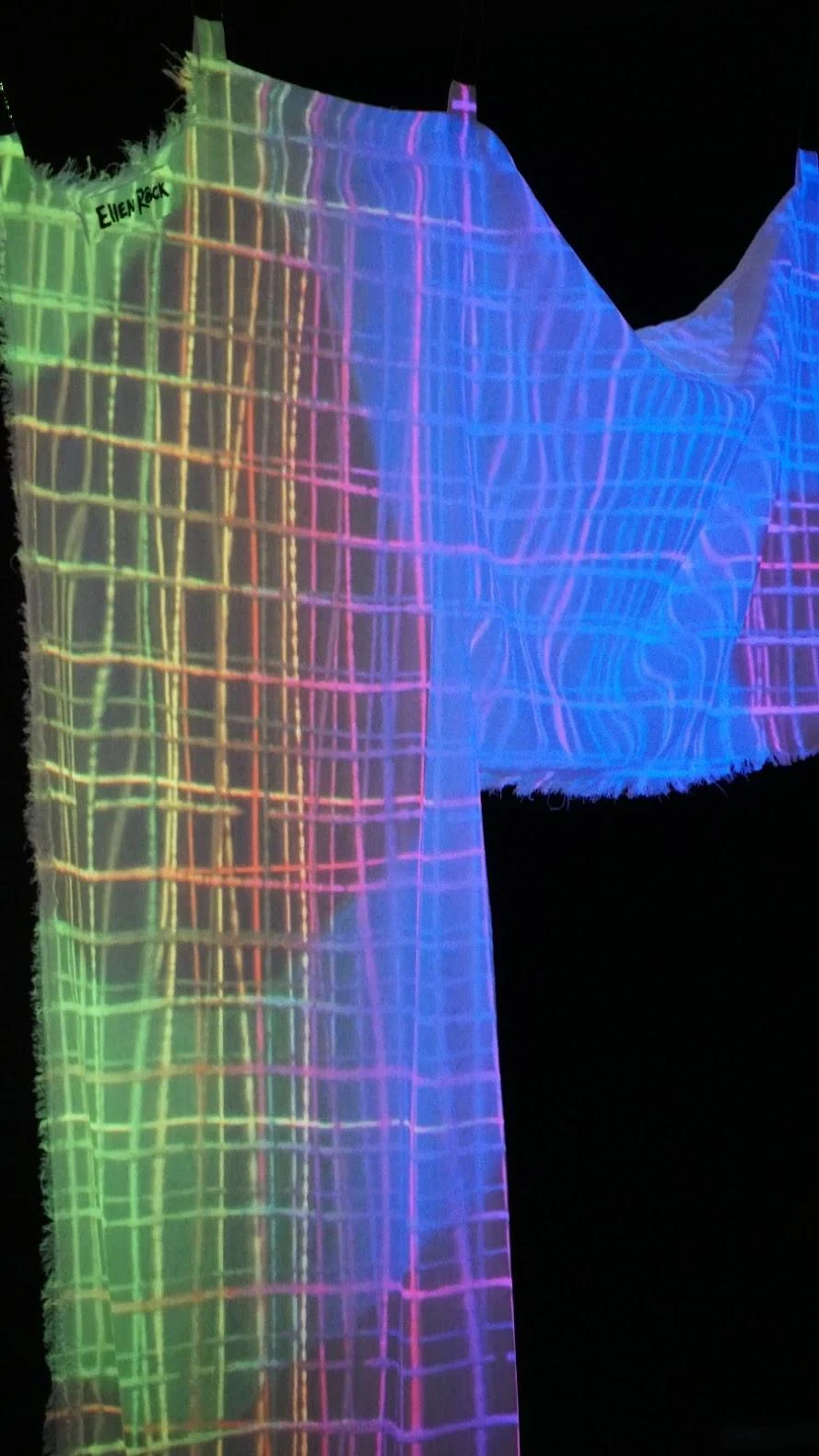 Multicoloured wireframe projection of a hanging garment against black.