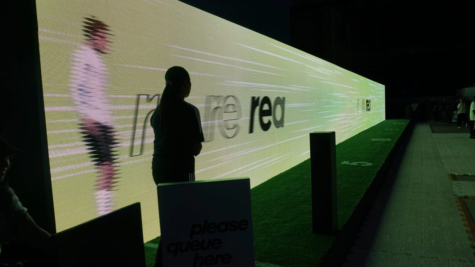Participant standing beside a long illuminated running wall at the Adidas X Crazyfast installation.