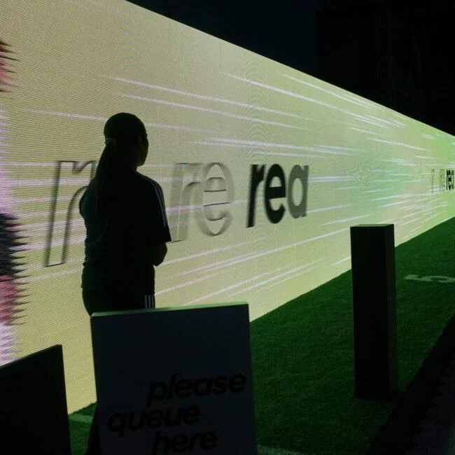 Participant standing beside a long illuminated running wall at the Adidas X Crazyfast installation.