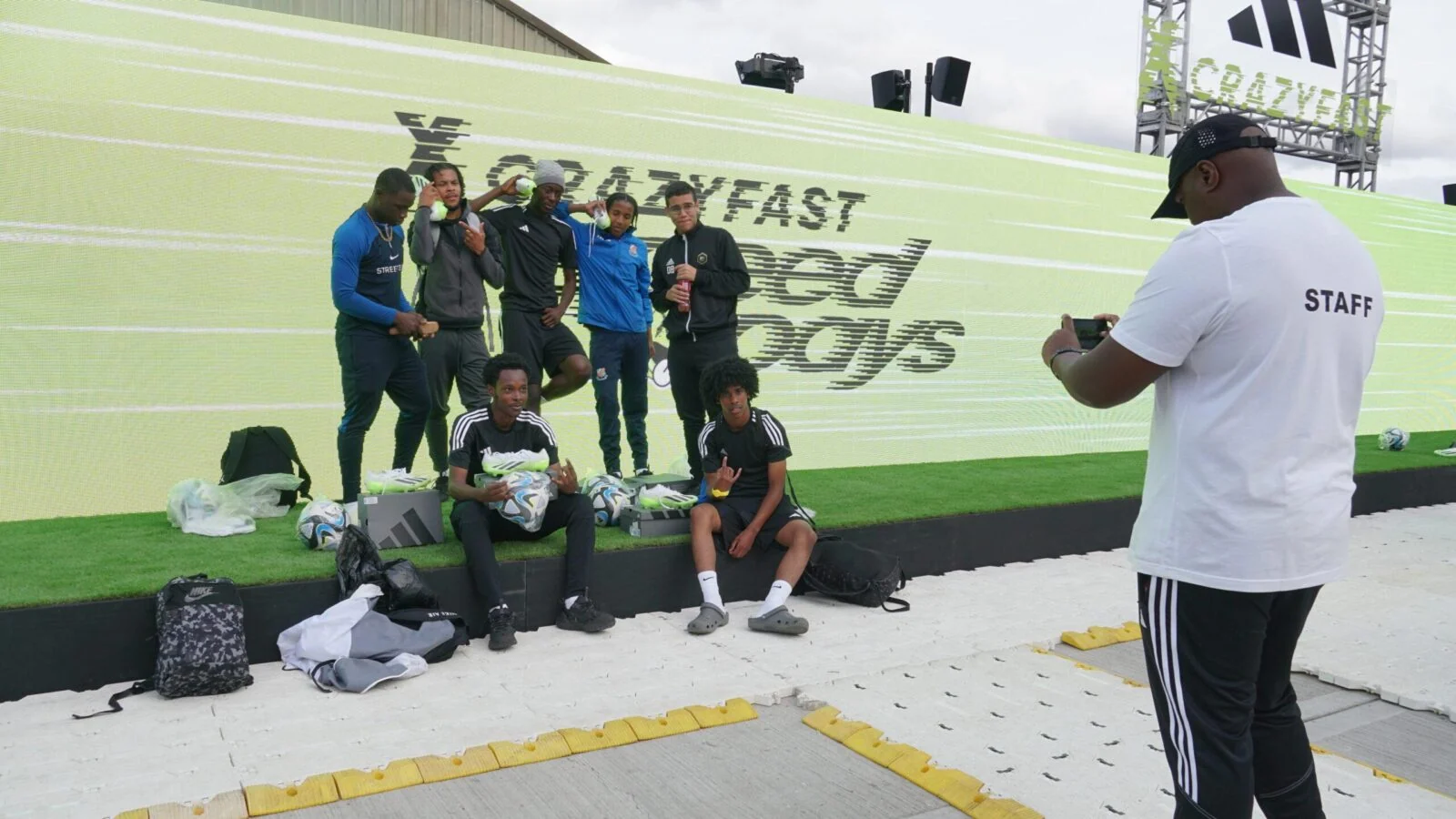 Group posing with footballs in front of the Adidas Crazyfast screen while a staff member takes a photo.
