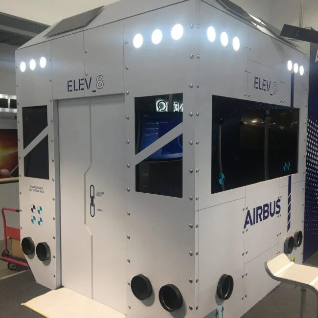 White Airbus ELEV8 exhibition cabin with illuminated upper panels and inset screens.