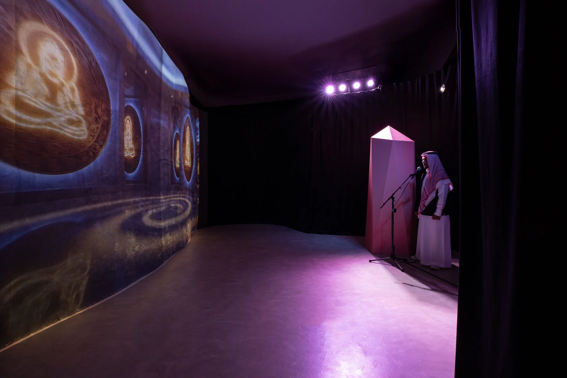 Curved projection wall and microphone station in the purple-lit Ascended Intelligence installation.