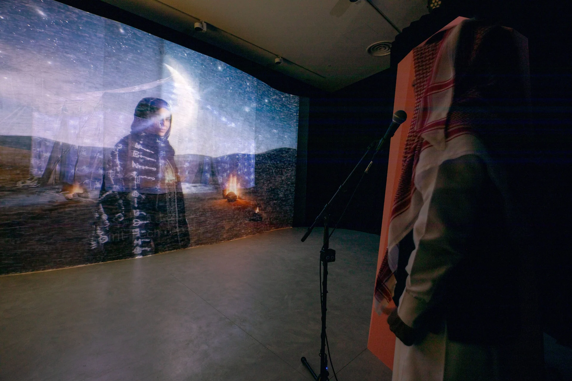 Visitor facing projected imagery and a microphone inside the Ascended Intelligence installation.