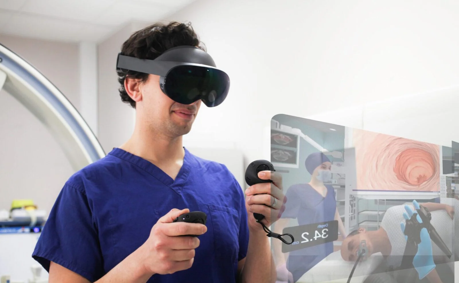 Person in blue scrubs wearing a VR headset and holding controllers beside an endoscopy simulation display.