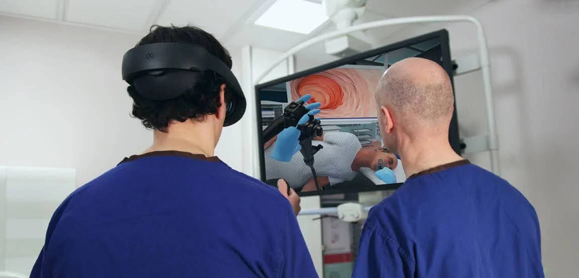 Two people in blue scrubs reviewing a VR endoscopy simulation on a monitor.