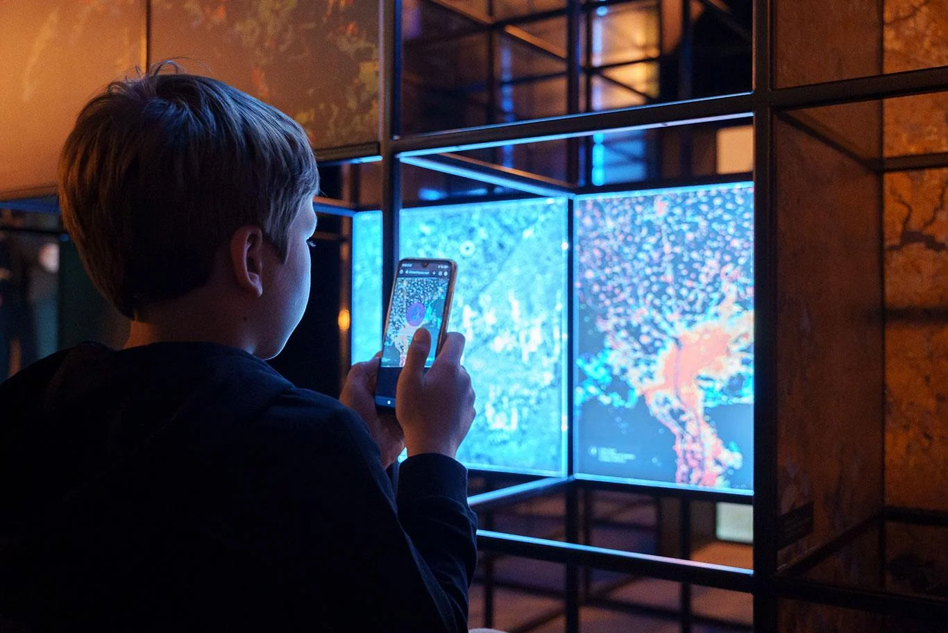 Visitor viewing a blue-lit Direction Earth/Space display through a smartphone.