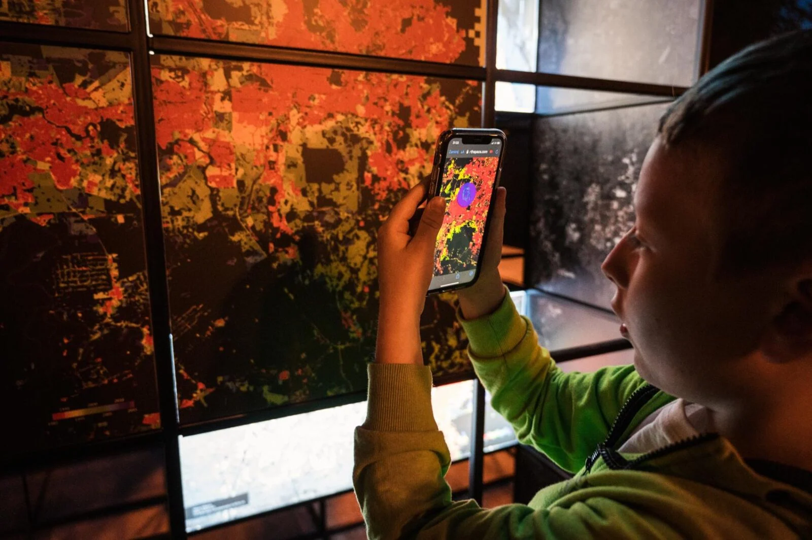 Visitor pointing a smartphone at a colourful Earth observation image in the outdoor exhibition.