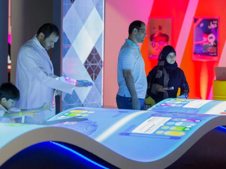 Visitors playing Energy Manager on a curved table covered with projected game graphics.