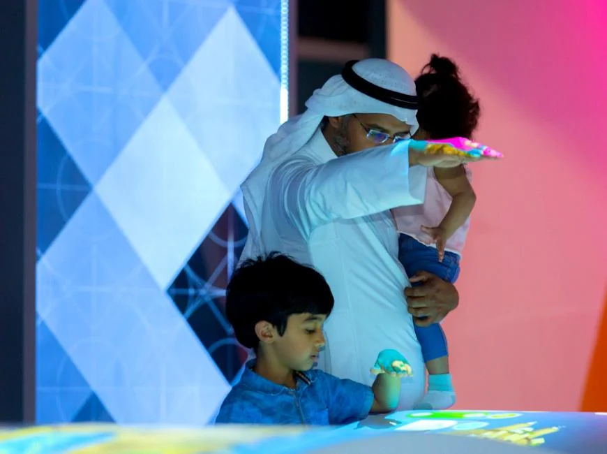 Adult holding a child while gesturing above the Energy Manager projection table.