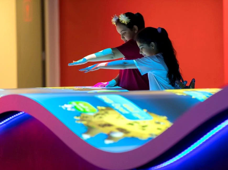 Two children extending their arms above the Energy Manager interactive table.