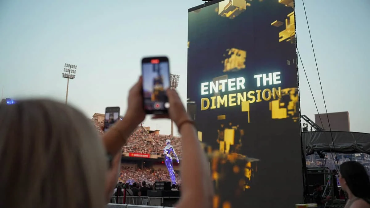 Concertgoer holding a phone towards a large Enter The Dimension screen.