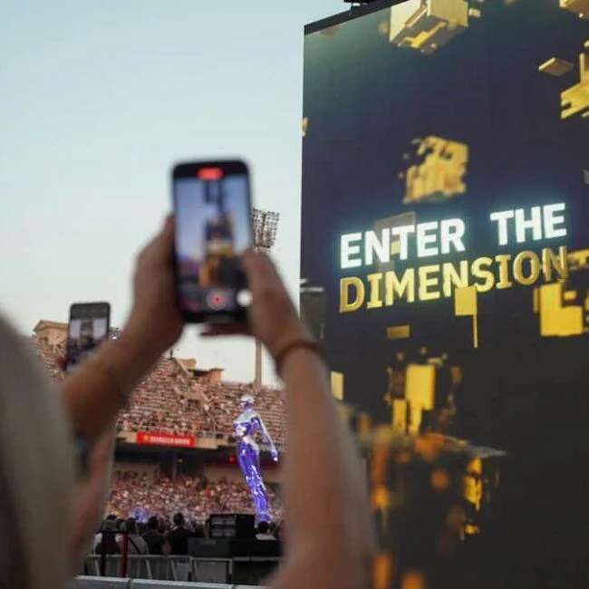 Concertgoer holding a phone towards a large Enter The Dimension screen.