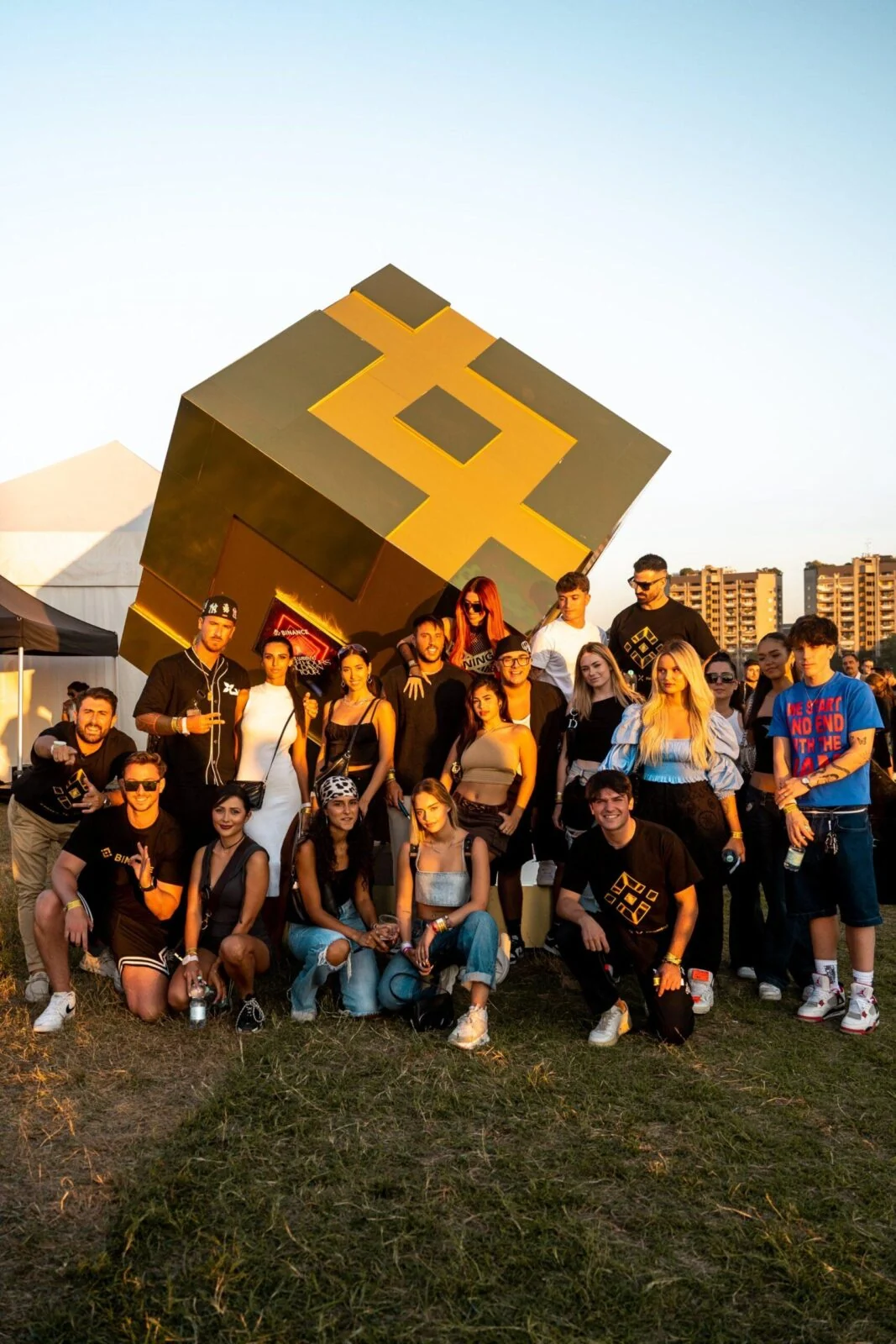 Group posing in front of a large gold Binance cube at an outdoor event.