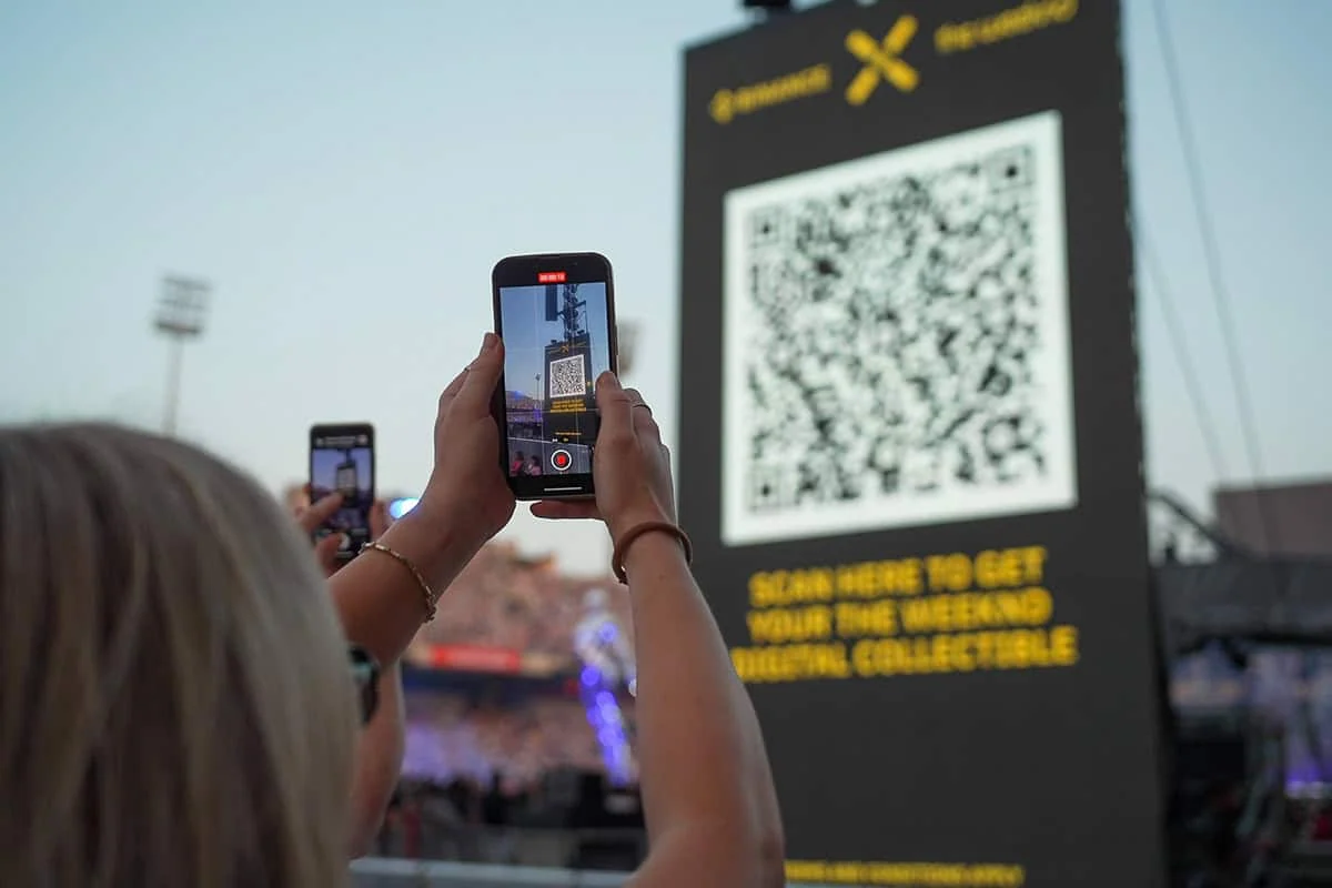 Concertgoer scanning a QR code on a Binance and The Weeknd event screen.