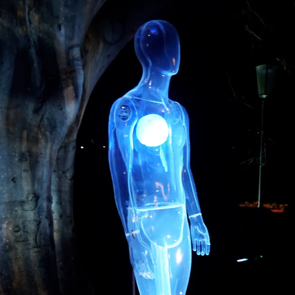 Transparent blue humanoid sculpture with a glowing white light in its chest.