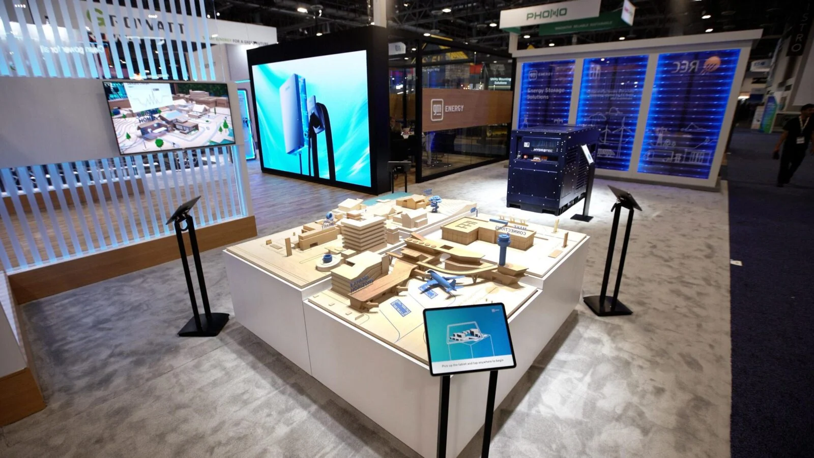 GM Energy exhibition stand with a model-city table, tablets and large display screens.