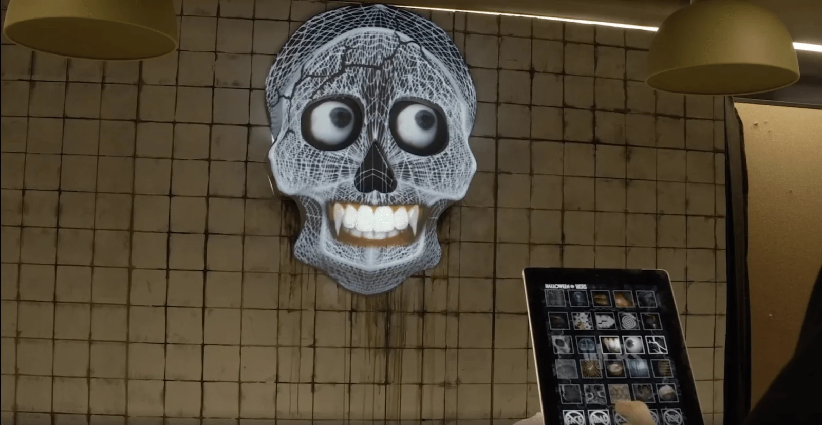 Grinning skull projection beside a tablet showing a grid of visual options.