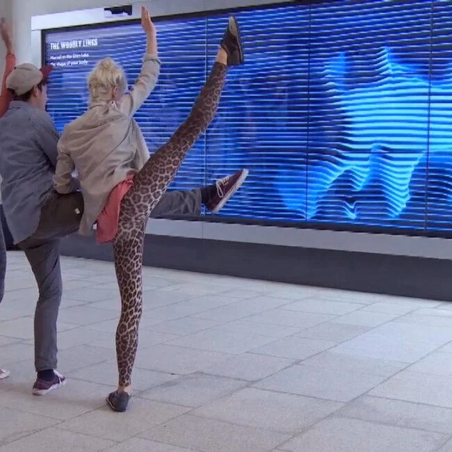 Visitors posing in front of a blue video wall that echoes their silhouettes.