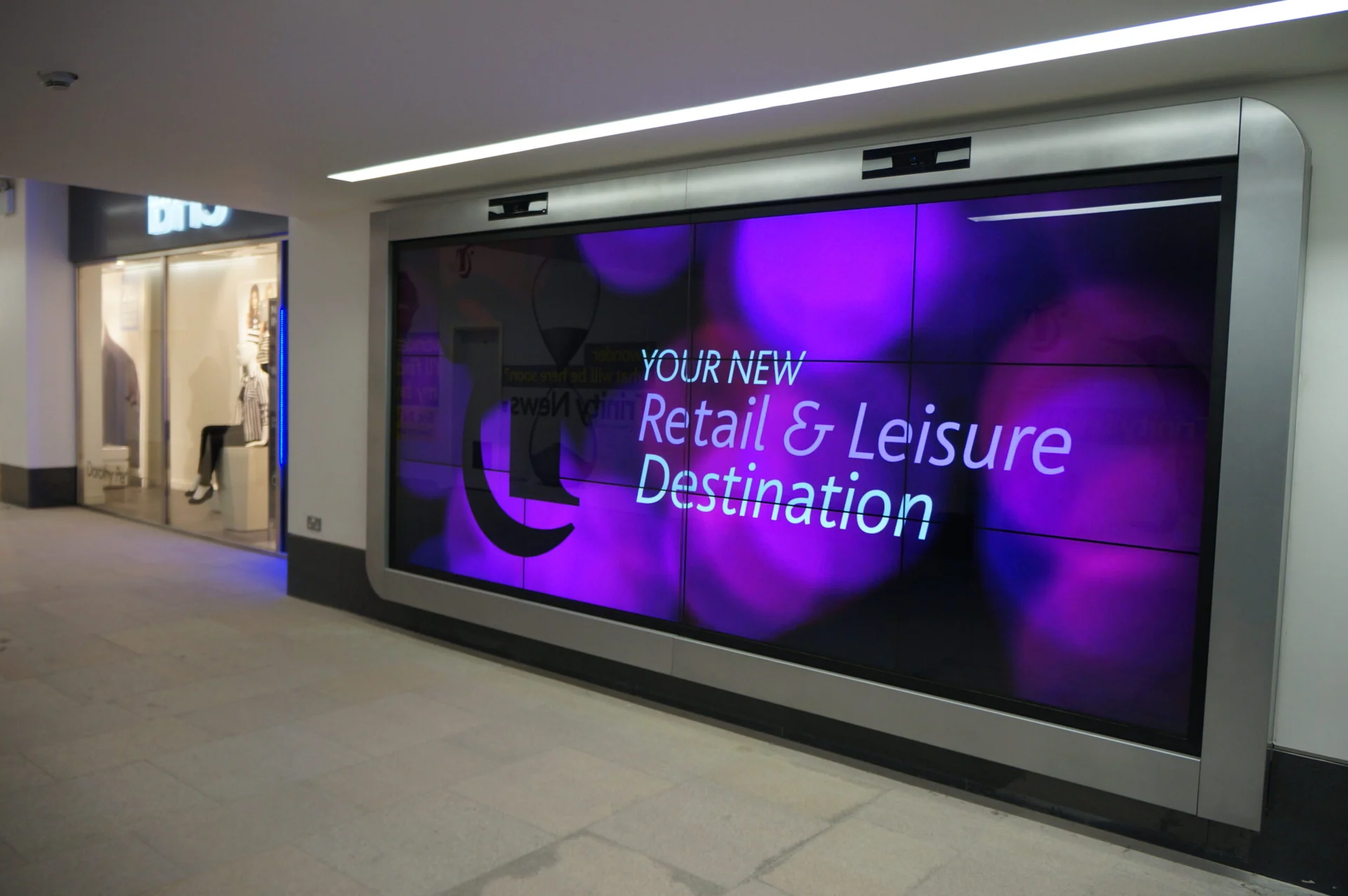 Large framed video wall displaying purple retail and leisure graphics in a shopping centre.