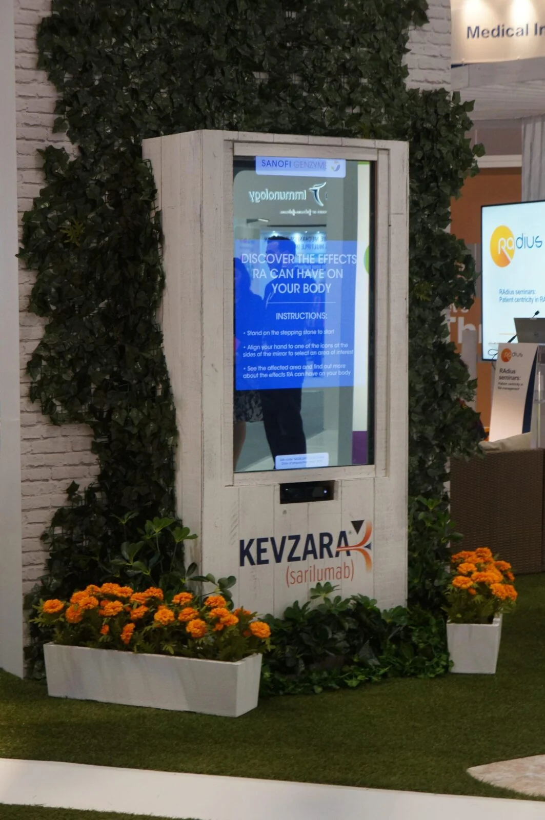 Interactive X-ray mirror kiosk set into a green plant wall at an exhibition stand.