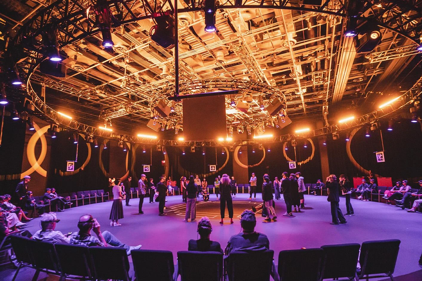Wide view of the Kagami venue with overhead lighting, circular graphics and visitors around the central floor.