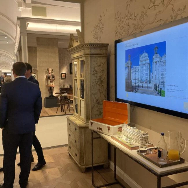 Visitors beside an architectural display screen and scale models at Masterpiece fair.