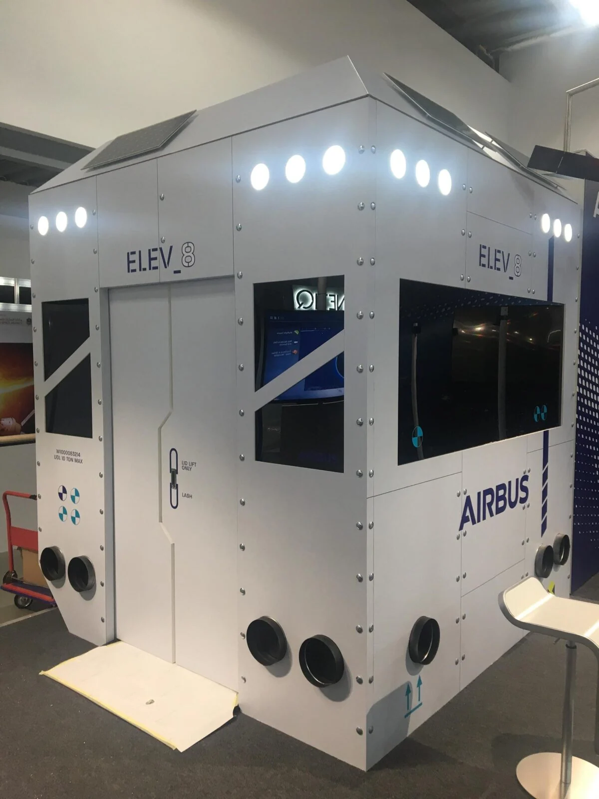 White Airbus ELEV8 exhibition cabin with illuminated upper panels and inset screens.