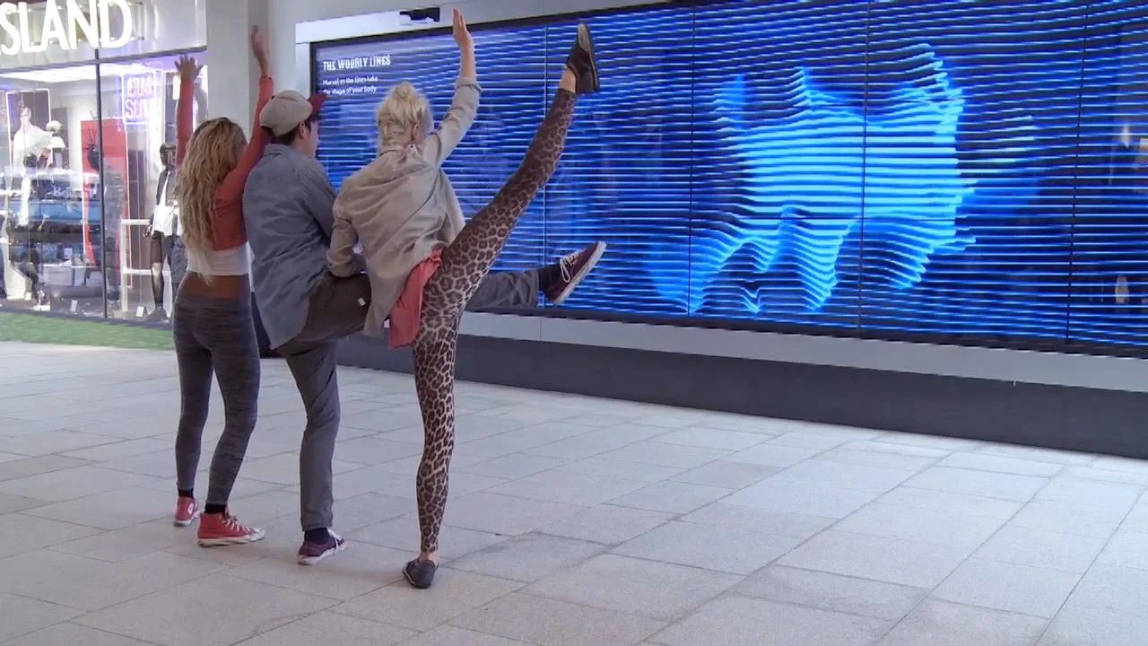 Visitors posing in front of a blue video wall that echoes their silhouettes.