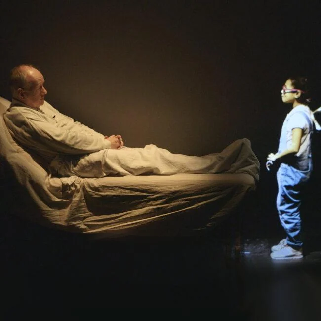 Bed and projected character in the mixed-media stage production The Fall.