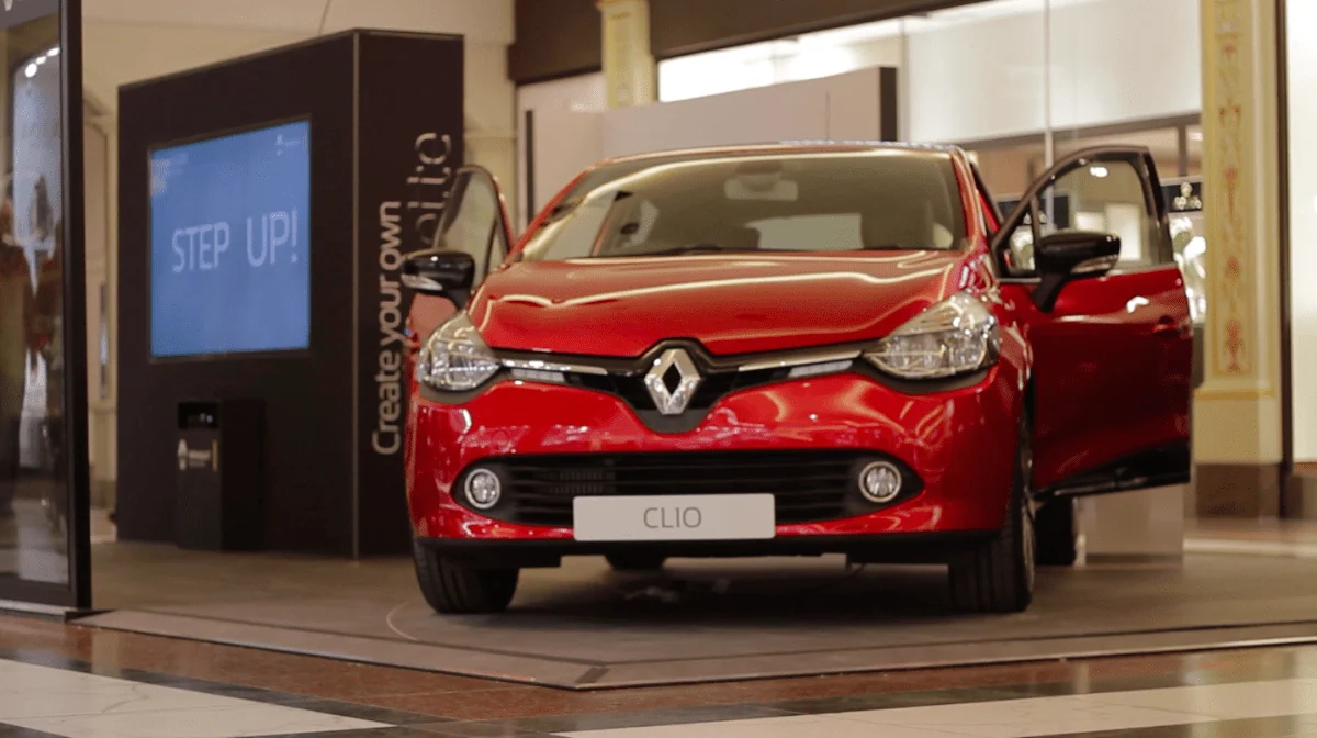 Red Renault Clio beside a Step Up interactive kiosk in a shopping centre.