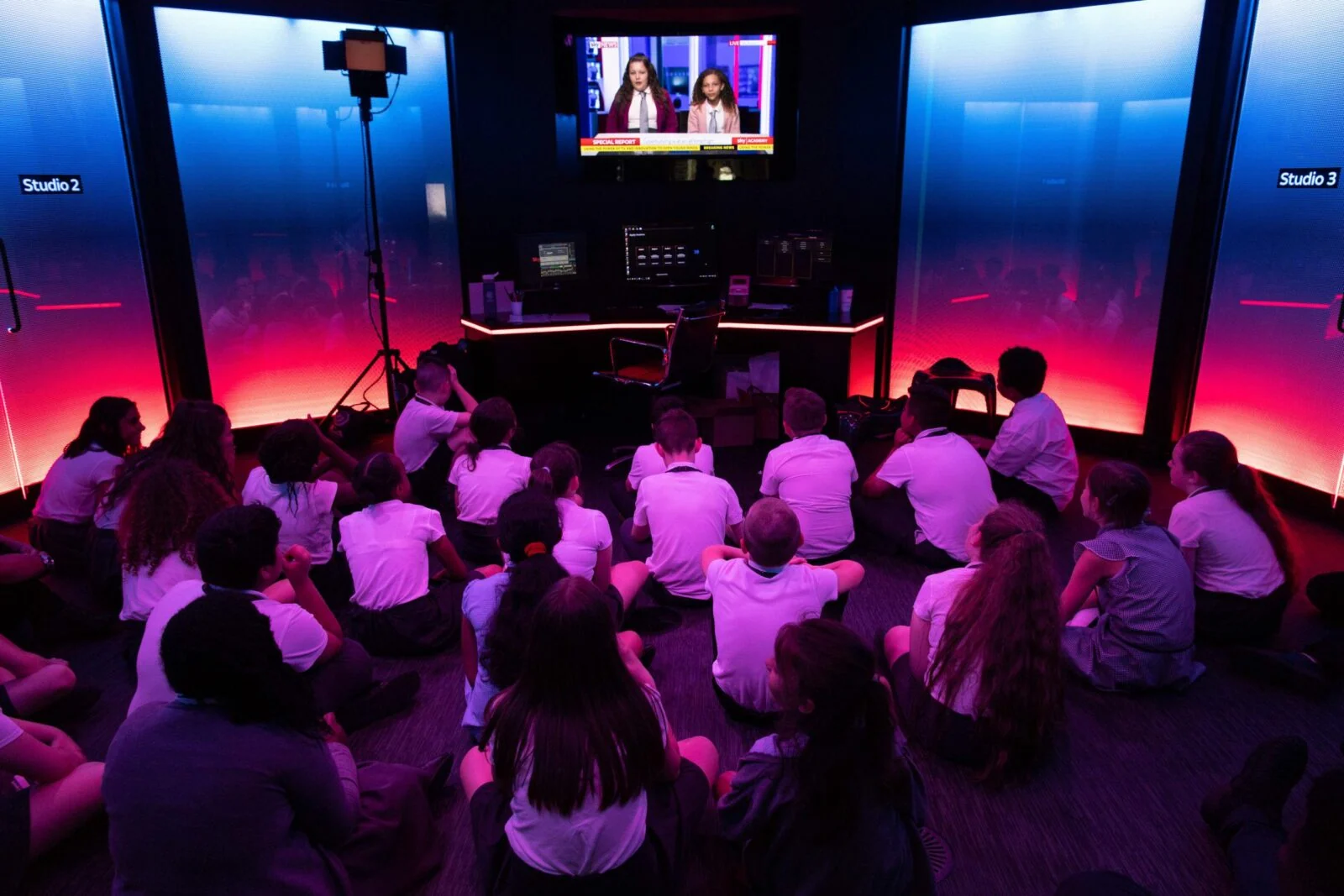Children seated on the floor watching a monitor in a brightly lit Sky Academy studio.