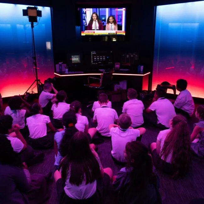 Group of children watching a studio monitor under blue and pink lighting.