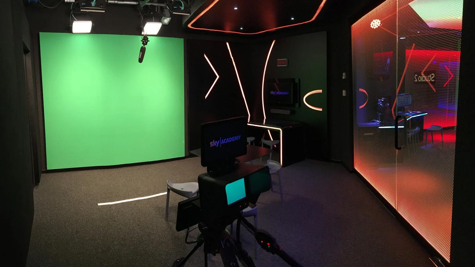 Studio camera facing a green screen beneath lights and a boom microphone.
