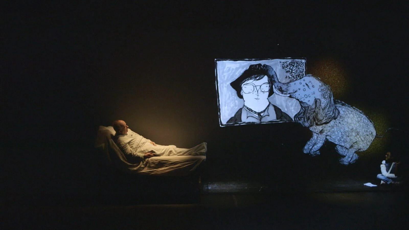Performer on a bed beneath large projected hand-drawn figures.