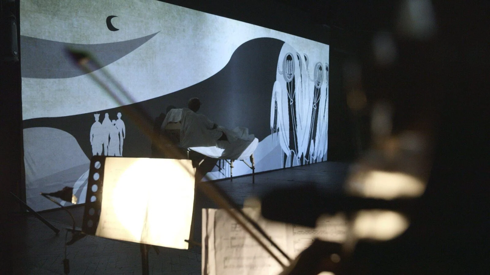 Stage projection of black-and-white illustrations with production equipment in the foreground.