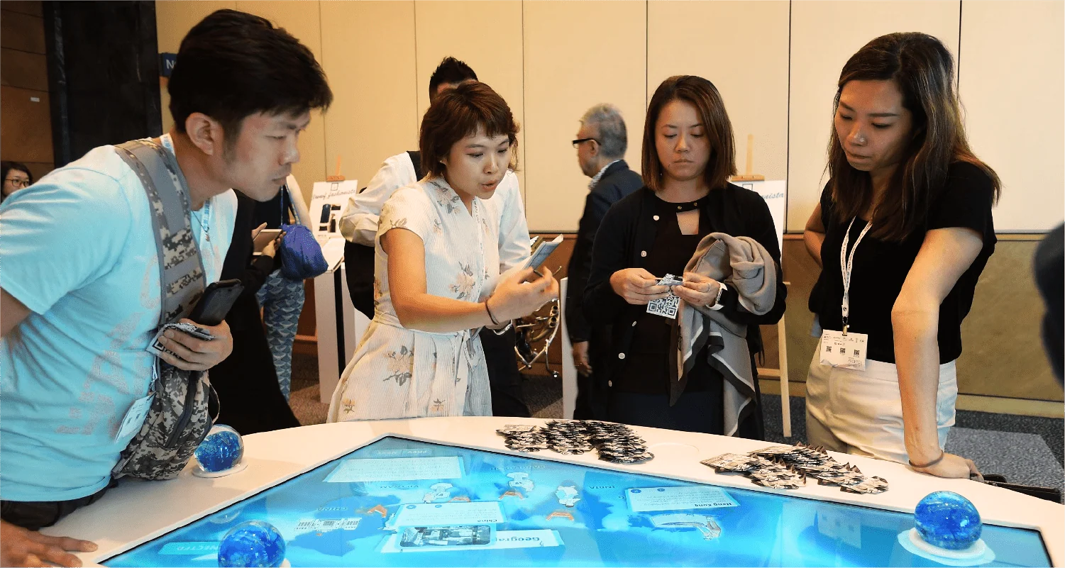 Visitors exploring a blue interactive tabletop with globe-shaped controls at a WaterAid event.