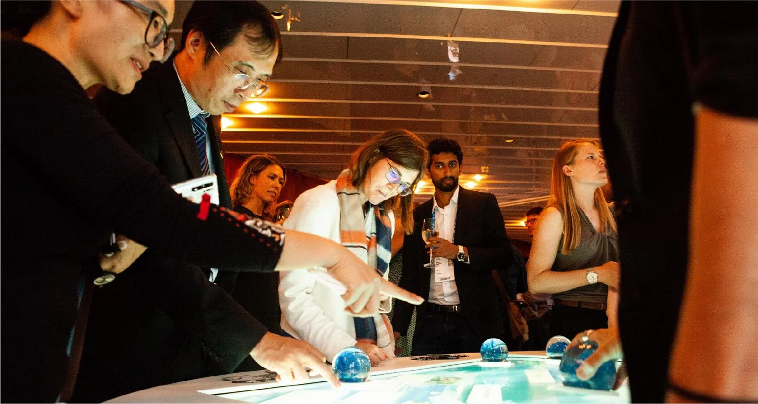 Event visitors moving globe-shaped objects on the illuminated WaterAid interactive table.