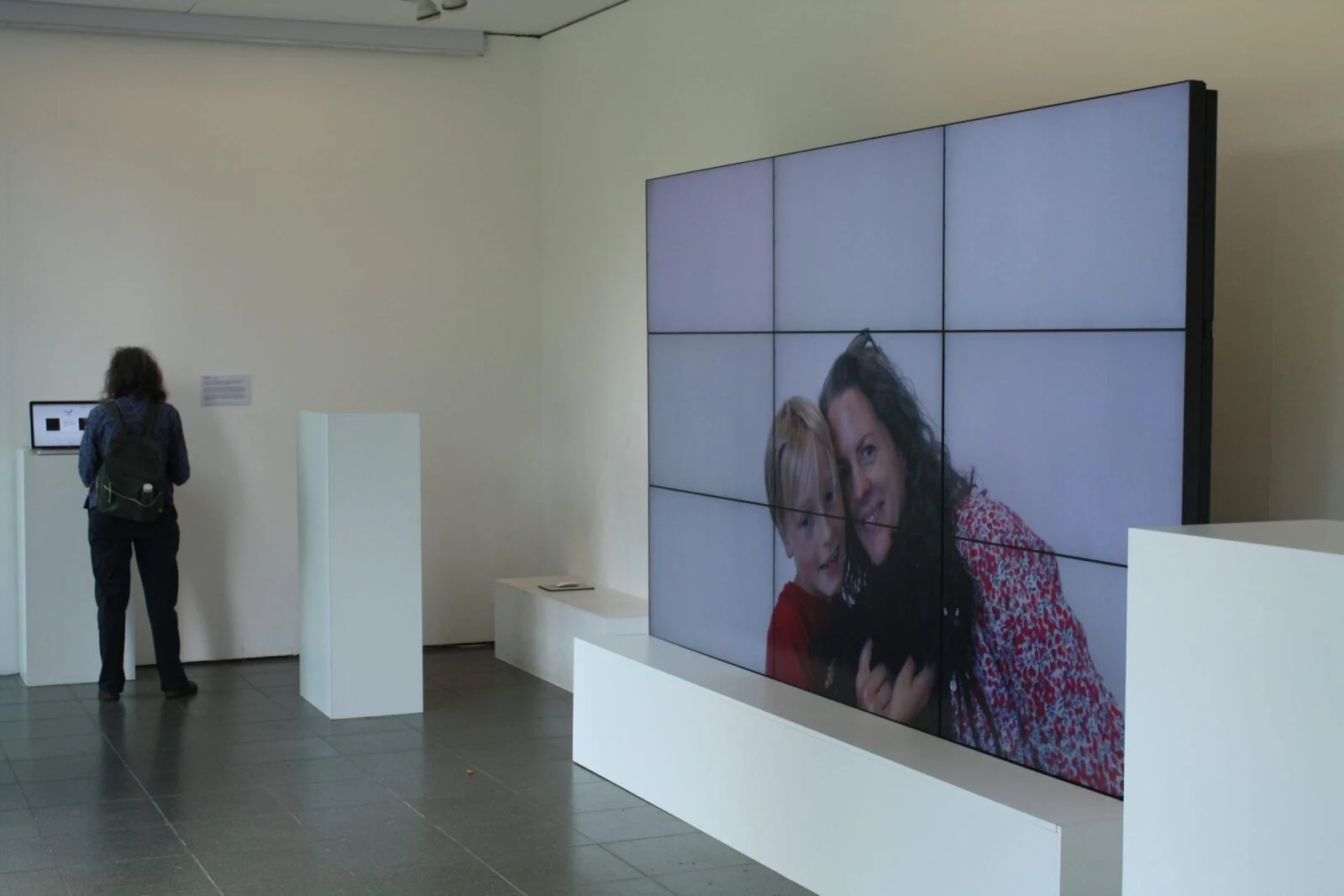 Gallery installation with a large video wall showing smiling participants.